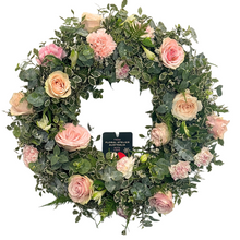 Load image into Gallery viewer, A round floral wreath with a variety of pink flowers, including roses and carnations, with green foliage.