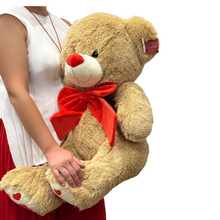Load image into Gallery viewer, Oversized 90 cm Teddy Bear Deluxe with soft beige fur, a bright red bow, and heart accents on its paws. This plush toy is perfect for making a bold, heartfelt statement on Valentine’s Day or paired with luxurious bouquets for an unforgettable gift.