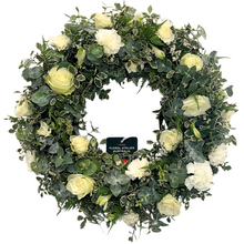 Load image into Gallery viewer, A medium-sized white floral wreath made with roses and carnations, surrounded by green foliage.