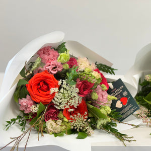 The Amore Bouquet in standard size, featuring Ferrari red roses, wine-toned blooms, and seasonal flowers, wrapped in white paper with velvet ribbons. Includes flower food for freshness.