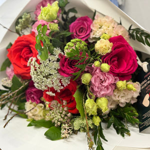 The Amore Bouquet Standard Size, featuring a greater number of Ferrari red roses and darker blooms, wrapped in white paper with velvet ribbons for a luxurious and romantic touch. Includes flower food for extended beauty.