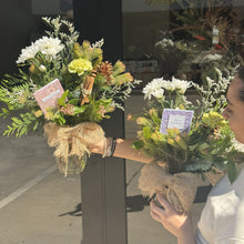 Load image into Gallery viewer, Two bouquets of Christmas flowers with ribbons held by a person, with a blurred background.
