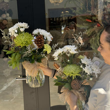 Load image into Gallery viewer, A person holding Christmas style flower bouquets in front of a glass door.

