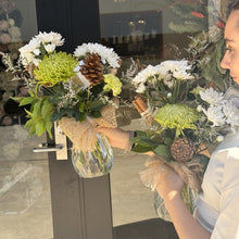 Load image into Gallery viewer, Person holding two Christmas bouquets of flowers in front of a door
