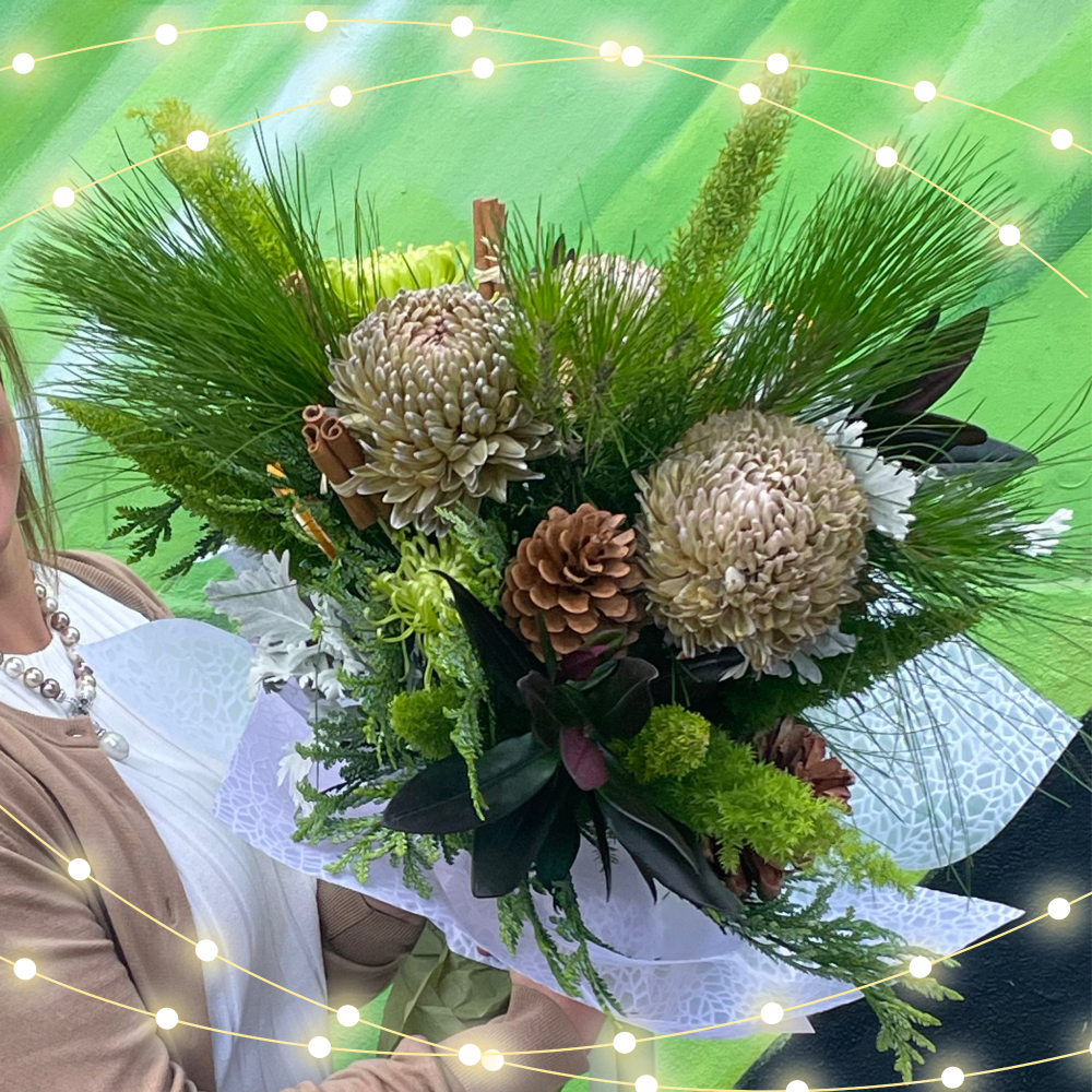 An earthy, nature-inspired Christmas bouquet with lush green foliage, large pine cones, and textured blooms in soft, neutral tones. This arrangement conveys a deep sense of connection, perfect for symbolizing unity and long-lasting relationships during the festive season.