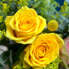 Load image into Gallery viewer, A close-up view of the Sunshine Rose Posy, showcasing vibrant yellow and pink roses arranged elegantly in a glass vase. The detailed shot highlights the delicate petals, lush greenery, and a bright yellow billy button at the center, capturing the fresh and lively essence of this cheerful arrangement.
