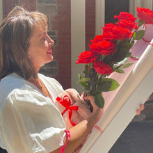 Load image into Gallery viewer, In a quiet Adelaide courtyard, she gazes at the Dozen Ferrari Red Roses, their beauty matched only by the tenderness with which she holds the plush bunny, a perfect endnote to Floral Atelier Australia&#39;s story of love, delivered with care and same day flower delivery
