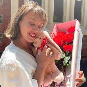 A gentle embrace with the soft plush bunny nestled against Floral Atelier Australia's Dozen Ferrari Red Roses, a picture of serenity and affection in Adelaide, perfectly capturing the essence of a heartwarming Valentine's Day surprise, ready for same day flower delivery