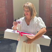 Load image into Gallery viewer, A moment of delight unfolds as she reads the love note accompanying Floral Atelier Australia&#39;s Dozen Ferrari Red Roses &amp; Plush Bunny in a Box, her smile reflecting the thoughtful gesture behind Adelaide&#39;s most cherished same day flower delivery service
