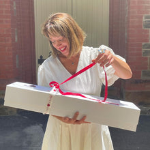 Load image into Gallery viewer, Joy is in the air as she playfully unravels the ribbon, teasing the surprise of the Dozen Ferrari Red Roses &amp; Plush Bunny in a Box, curated with care by Floral Atelier Australia and ready for same day delivery to share the love in Adelaide

