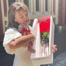 Load image into Gallery viewer, Savoring the joy of discovery, she holds the plush bunny close, with the Dozen Ferrari Red Roses box open before her, a moment treasured and made possible by Floral Atelier Australia, Adelaide&#39;s premier choice for heartfelt expressions and same day flower delivery
