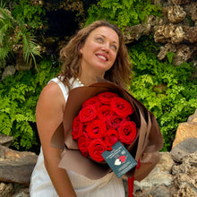 Load image into Gallery viewer, A tender moment as a woman admires the Elegant 12 Ferrari Red Roses Bouquet, handcrafted by Floral Atelier Australia, against a verdant rocky backdrop, perfect for expressing love with Adelaide&#39;s renowned same day flower delivery service
