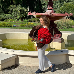 Beside the serene fountain in Adelaide, a woman is captivated by the Elegant 50 Ferrari Red Roses Bouquet from Floral Atelier Australia, showcasing a fusion of natural beauty and floral artistry, ready for same day flower delivery by Adelaide's premier florist