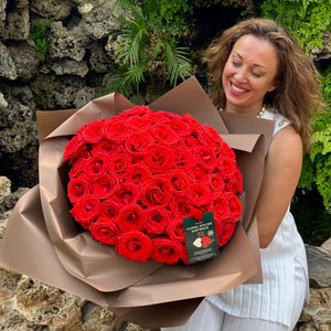 A woman's radiant smile complements the lush vibrancy of Floral Atelier Australia's Elegant 50 Ferrari Red Roses Bouquet, a testament to skilled craftsmanship, delivered with love in Adelaide for those special moments that demand a touch of luxury and same day flower delivery