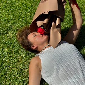 A serene moment captured with Floral Atelier Australia's Elegant Ferrari Red Rose, gracefully held by a woman relaxing on the lush Adelaide greens. This single red rose, ideal for conveying deep sentiments, is available with same day flower delivery from Adelaide's finest florist
