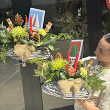 Load image into Gallery viewer, Decorative floral Christmas  arrangement with candles and a bow on a stand, held by a person.
