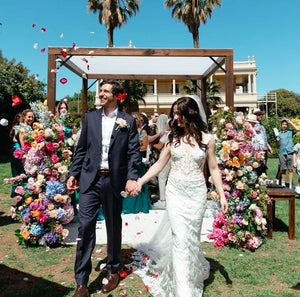 Bride and groom walking through mixed rose petal confetti tossed by guests, using 1 bag of fresh mixed petals from Floral Atelier Australia.