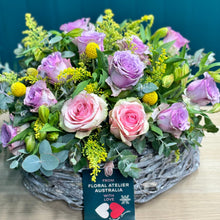 Load image into Gallery viewer, A lavish pastel rose arrangement in a glass vase with 2 pink roses, 10 purple roses, 5 alstroemerias, 4 yellow billy buttons, and rich foliage of golden rod and blue gum. The deluxe size showcases a fuller, more vibrant display, ideal for making a bold and elegant statement.
