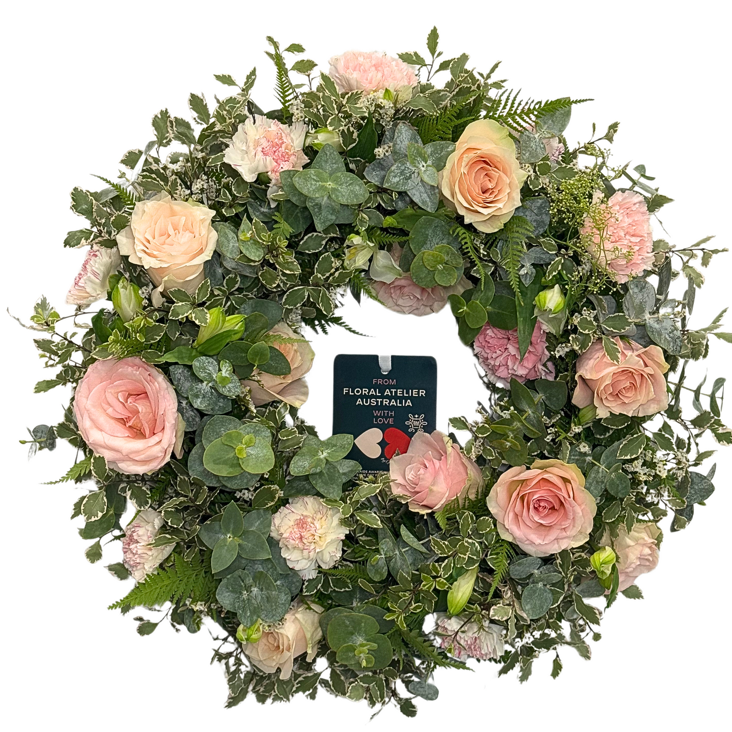 A round floral wreath with a variety of pink flowers, including roses and carnations, with green foliage.