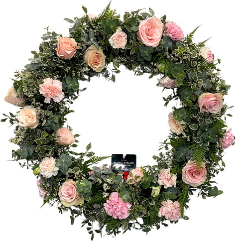 A round floral wreath with a variety of pink flowers, including roses and carnations, with green foliage.