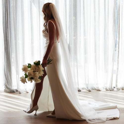 Bride in a white wedding dress with a long veil standing in front of sheer curtains and holding Reflexed White Ecuador Rose Bridal Bouquet made by Adelaide wedding Florist Floral atelier Australia.