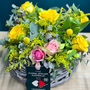 A vibrant arrangement of pink and yellow roses, accented with alstroemerias, yellow billy buttons, golden rod, and blue gum, creating a cheerful display in a standard size.