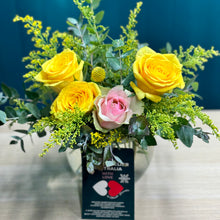 Load image into Gallery viewer, A delightful mini arrangement of yellow and pink roses, featuring a single pink rose surrounded by three bright yellow roses, accented with a yellow billy button and lush greenery, all elegantly arranged in a small glass vase.
