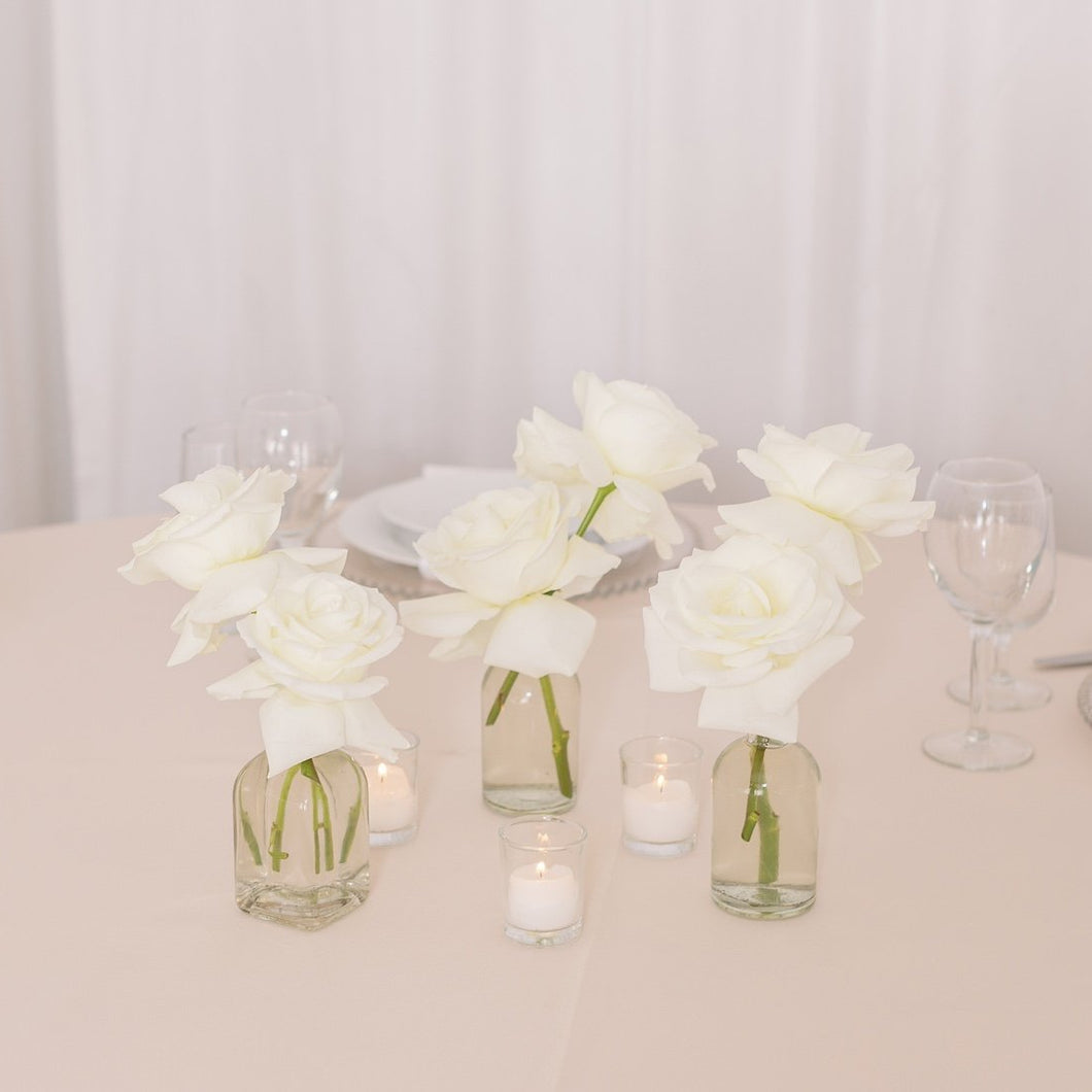 Trio of white roses in bud vases with votive candles and white rose petals – Floral Atelier Australia, Adelaide wedding florist.