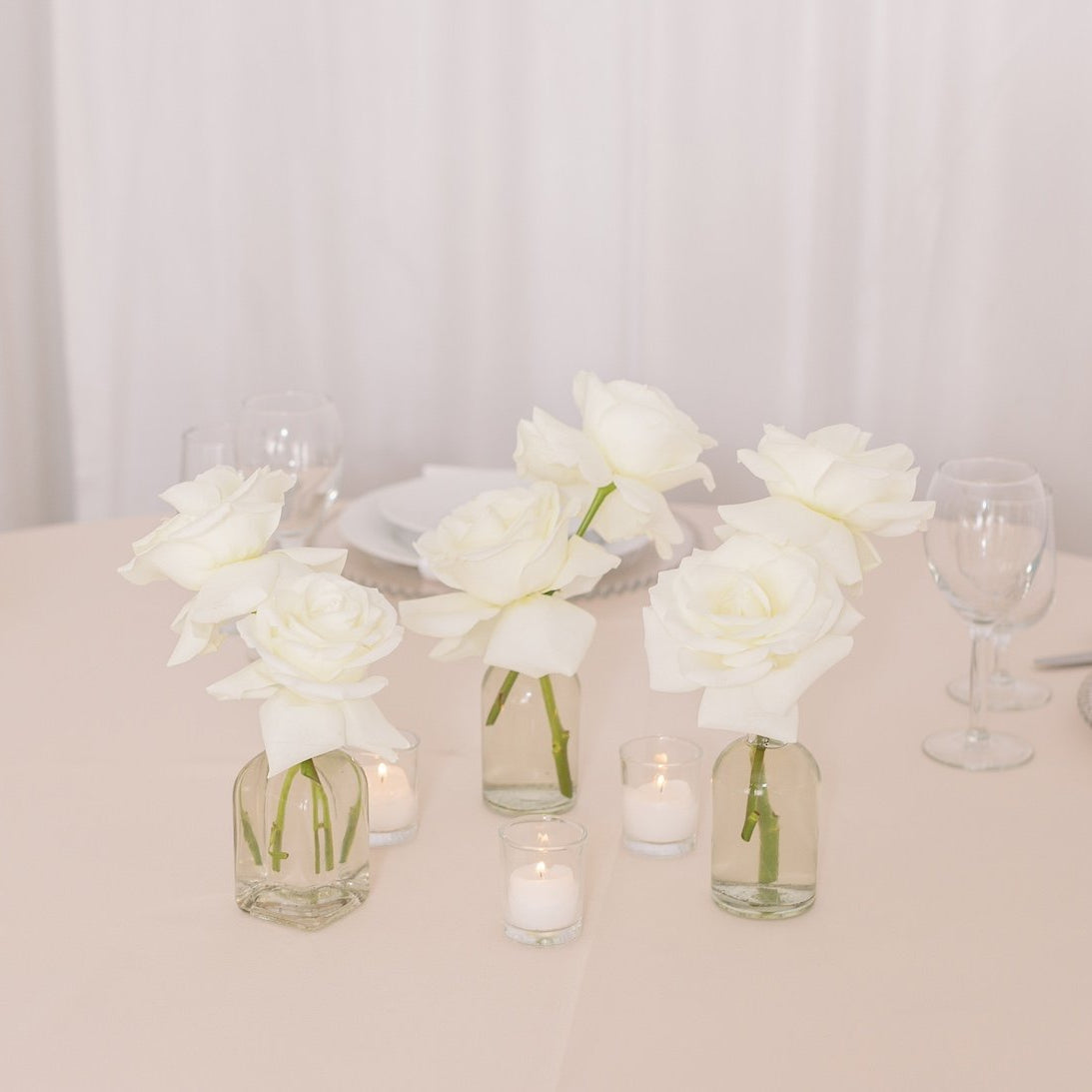Trio of white roses in bud vases with votive candles and white rose petals – Floral Atelier Australia, Adelaide wedding florist.