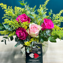 Load image into Gallery viewer, A vibrant rose posy in a glass vase featuring 1 pink rose, 3 hot pink roses, 1 yellow billy button, and lush accents of golden rod and blue gum. The mini size offers a compact yet lively display, perfect for adding a pop of color and cheer to any space.
