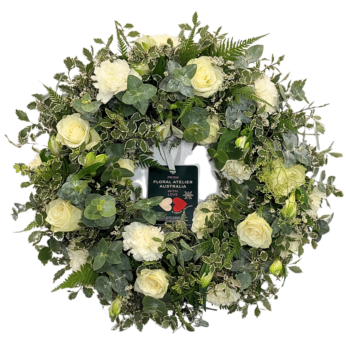 A medium-sized white floral wreath made with roses and carnations, surrounded by green foliage.