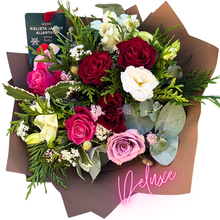 Load image into Gallery viewer, A luxurious, large bouquet showcasing an abundant mix of classic roses and seasonal flowers in vibrant red, soft pink, and subtle hues. Enhanced with lush greenery and wrapped in chocolate brown paper, this bouquet makes a bold, memorable statement.
