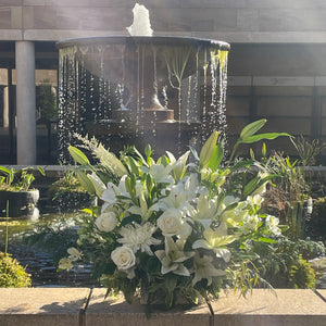 A lavish and grand arrangement of white flowers and abundant greenery, showcasing the Pure Life Arrangement in deluxe size. Perfect for conveying heartfelt condolences with its impressive and dignified display