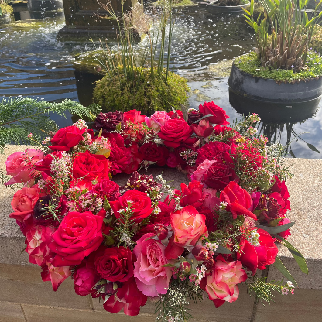 Red Rose Wreath placed at Pasadena Cemetery with a peaceful waterfall in the background, creating a serene and respectful atmosphere.