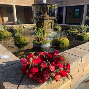 Elegant Red Rose Wreath displayed at Pasadena Cemetery, set against the tranquil backdrop of nature and a calming waterfall, symbolizing peace and remembrance.