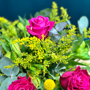 A detailed close-up of a vibrant floral arrangement with pink and hot pink roses, complemented by bright yellow billy buttons and rich greenery. The arrangement exudes a lively and cheerful essence, perfect for any joyful celebration.